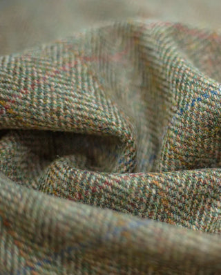 Detailaufnahme des Harris Tweed Stoffs light green herringbone, wo man gut die Musterschüsse in Rot, Blau und Gelbgold erkennt.