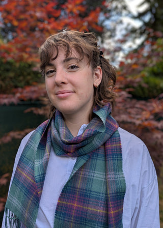 Der klassische Lammwollschal im Tartan Hame (Lindgrün, Blau, Lila mit schmalen gelben Linien) wird von unserem Model Anna getragen.